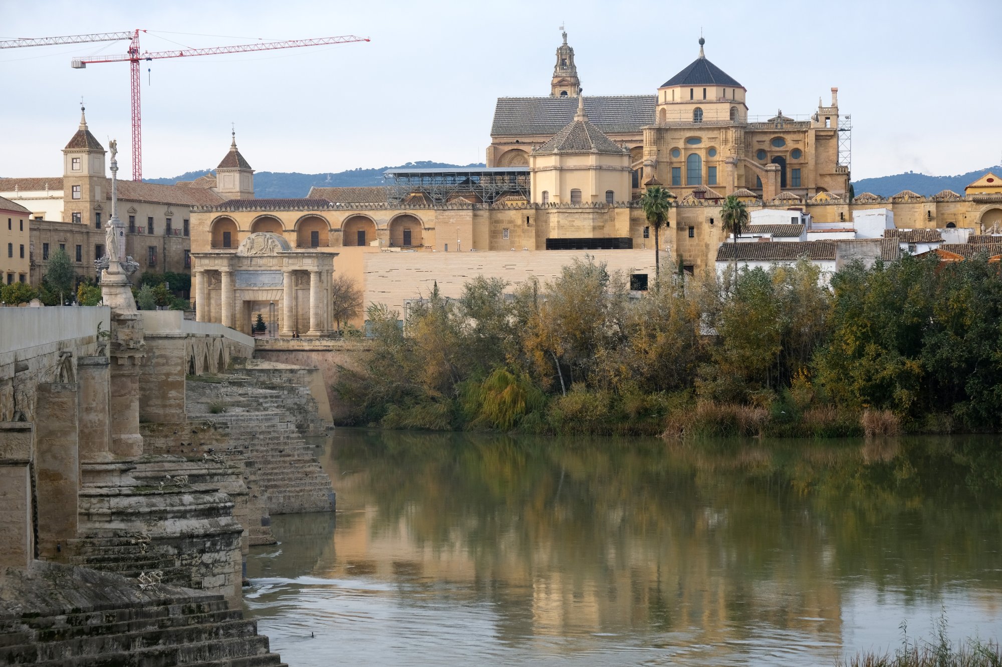 The Mosque-Cathedral of Cordoba and its bell tower above the Guadalquivir, seen from the Roman bridge end on a grey December afternoon, with a construction crane behind