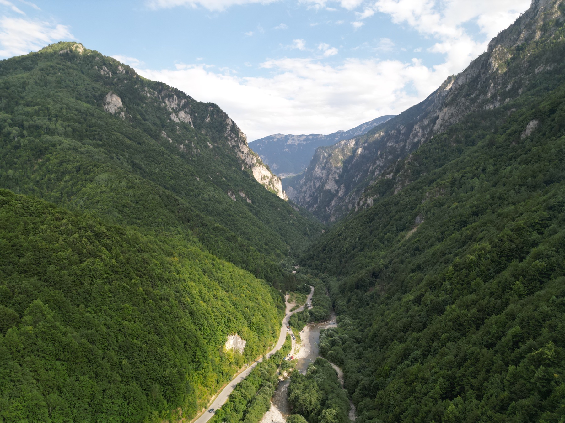 Aerial view of a road and river winding between forested cliffs in Rugova Canyon