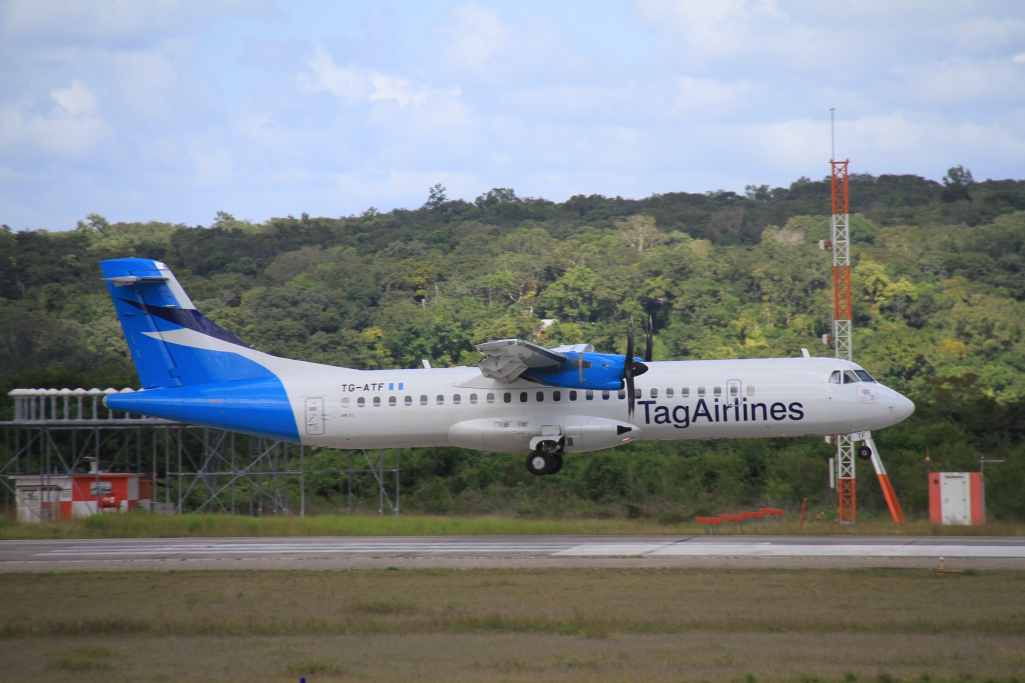 A TAG Airlines ATR 72 turboprop touching down on the runway at Mundo Maya International Airport near Flores with trees behind
