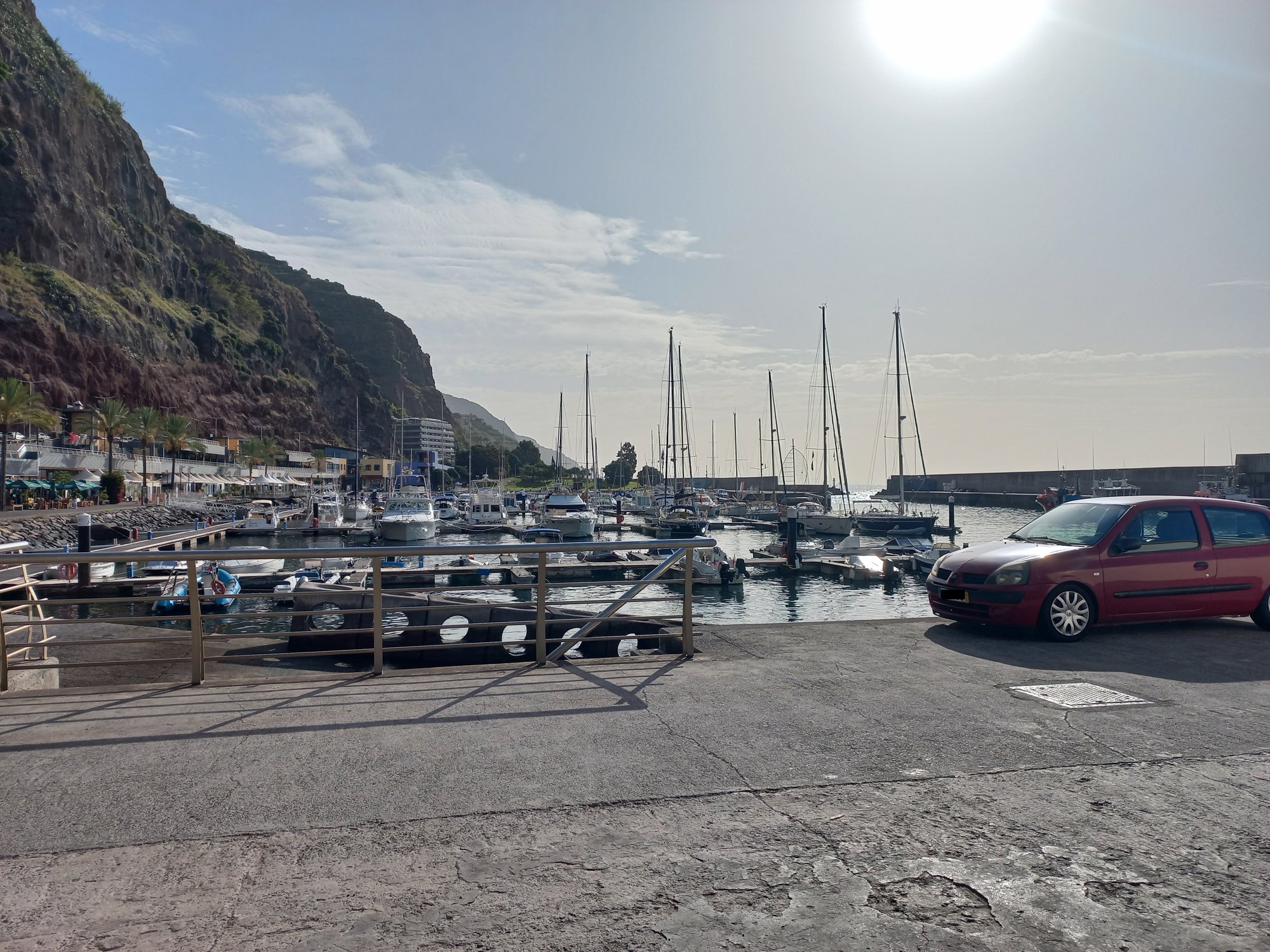 Yachts and small boats in Calheta marina backed by steep cliffs, photographed into a hazy sun