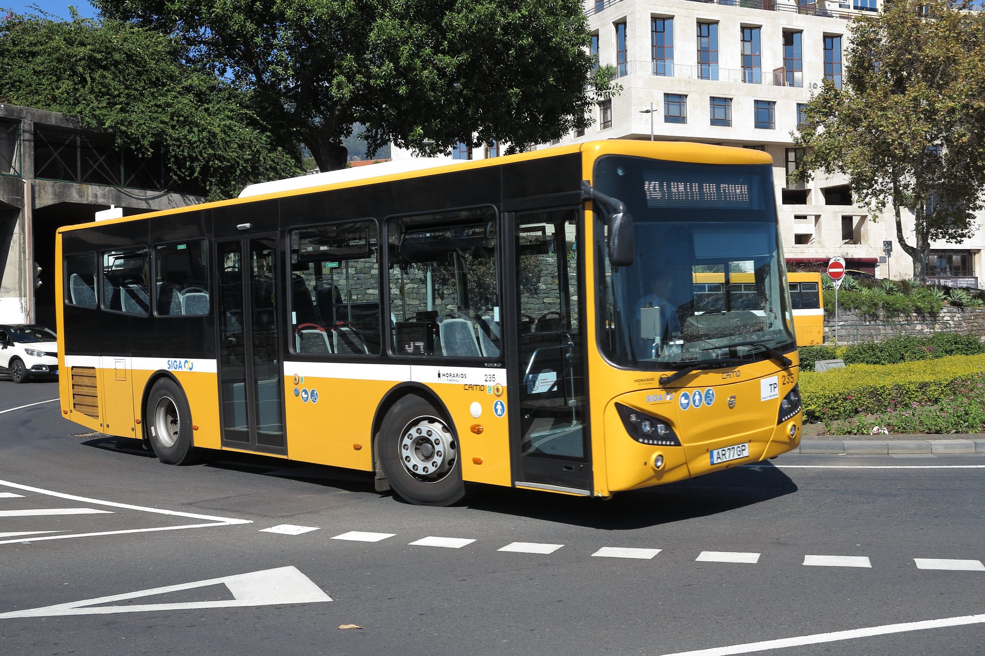 A yellow SIGA network city bus turning at a junction in Funchal