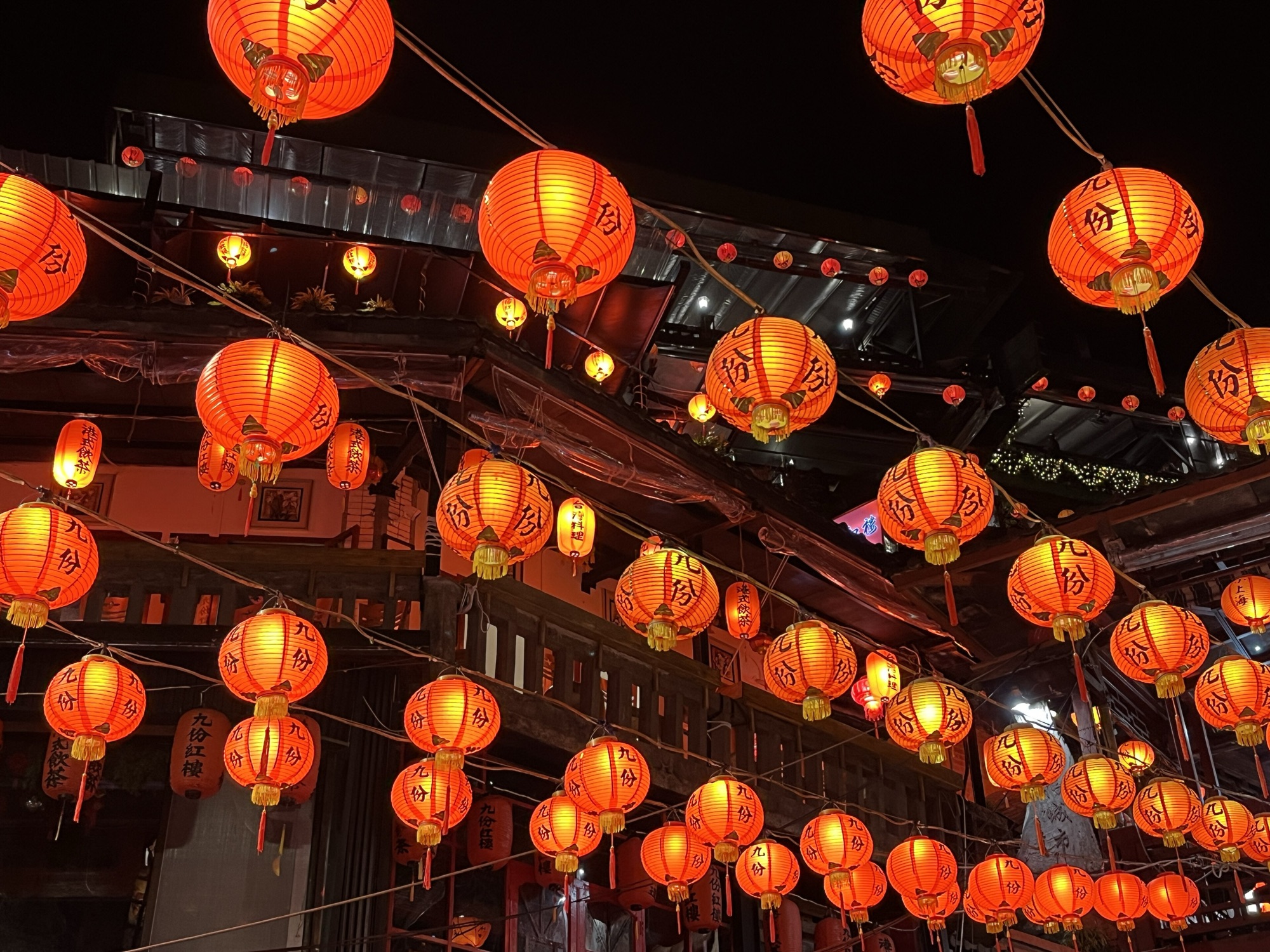 Dozens of glowing red paper lanterns strung above the wooden tea houses of Jiufen Old Street at night
