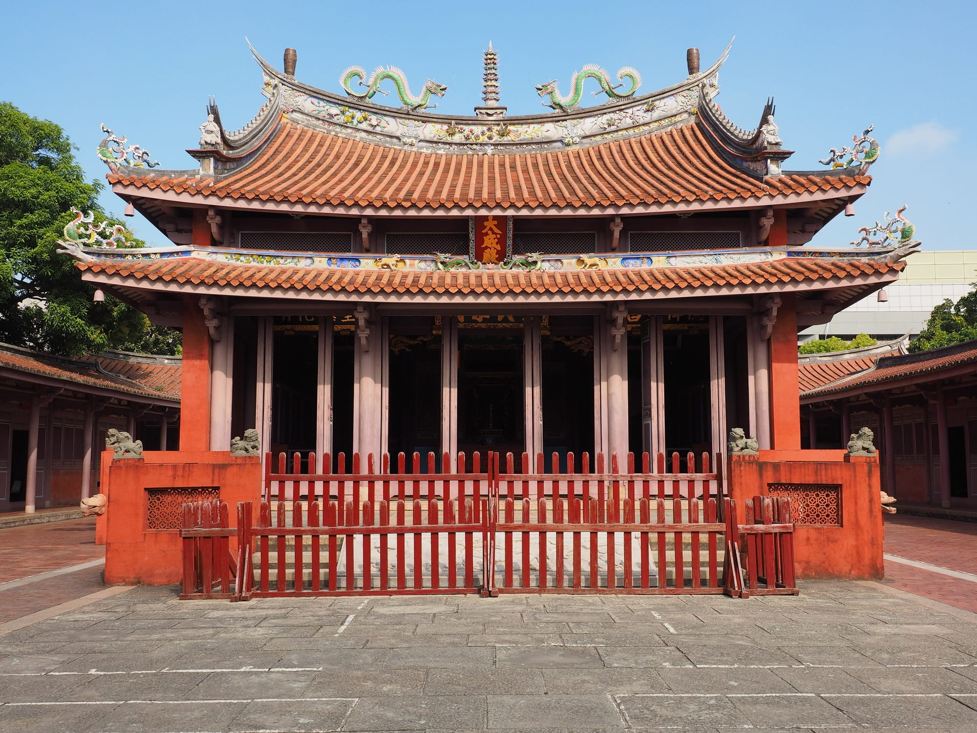 The red-walled Dacheng Hall of the Tainan Confucius Temple with its double-eaved tiled roof and stone courtyard under a clear sky