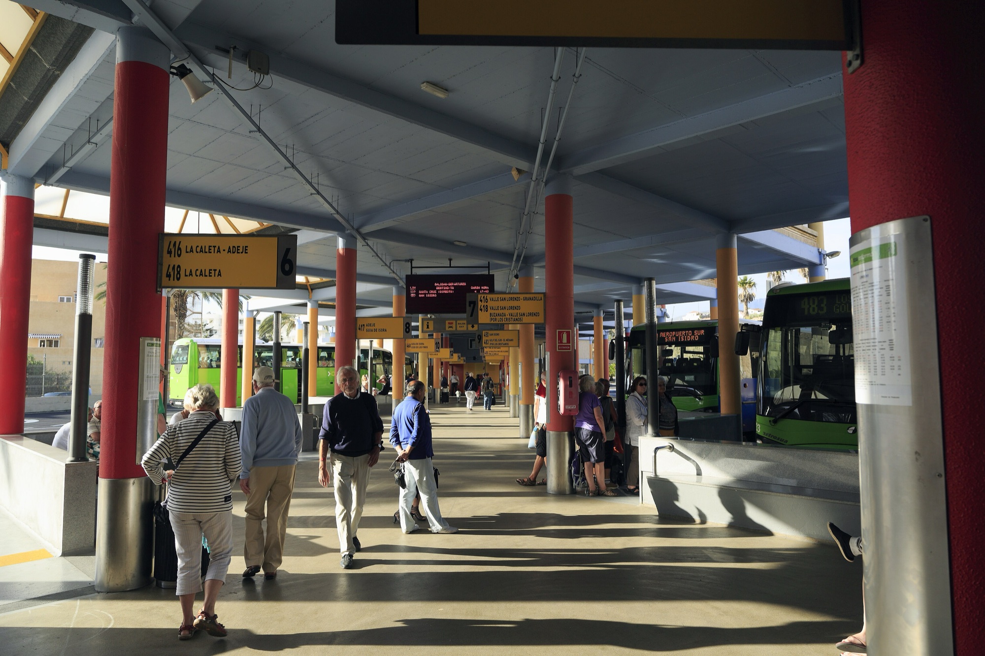 Covered platforms of the Costa Adeje bus station with passengers and green TITSA buses
