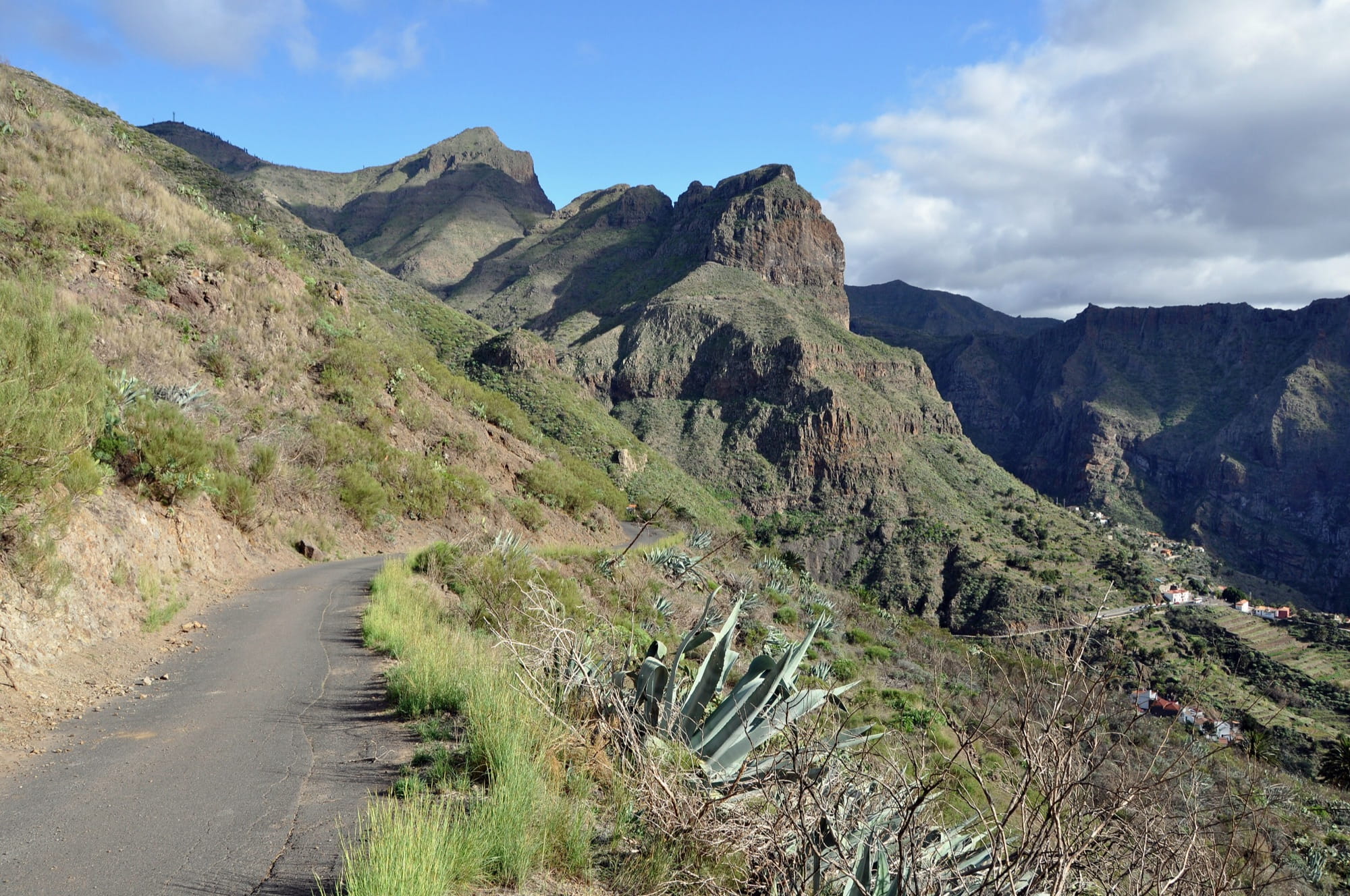 Narrow mountain road curving towards the jagged Teno peaks with the houses of Masca hamlet in the valley below
